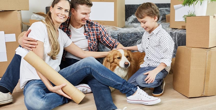 family sitting on the ground next to moving boxes and their dog