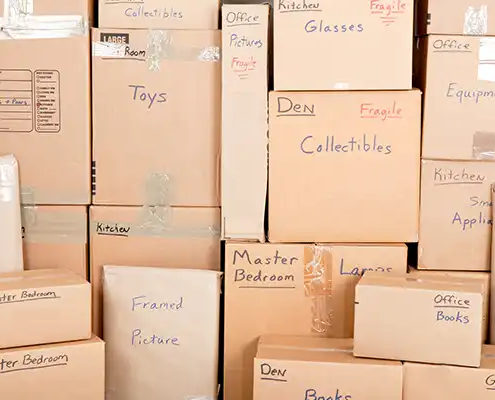 an assortment of stacked los angeles moving boxes labeled: toys, den, office, master bedroom, framed, collectibles, fragile, equipment, kitchen, small appliances, large, medium, pots, pans