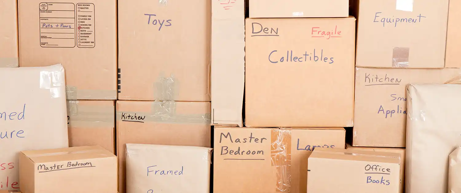 an assortment of stacked los angeles moving boxes labeled: toys, den, office, master bedroom, framed, collectibles, fragile, equipment, kitchen, small appliances, large, medium, pots, pans