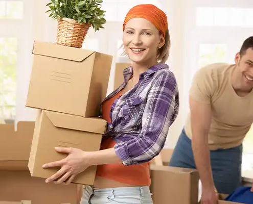 woman holding boxes while short distance moving. a man is in the background. both are looking at the camera smiling.
